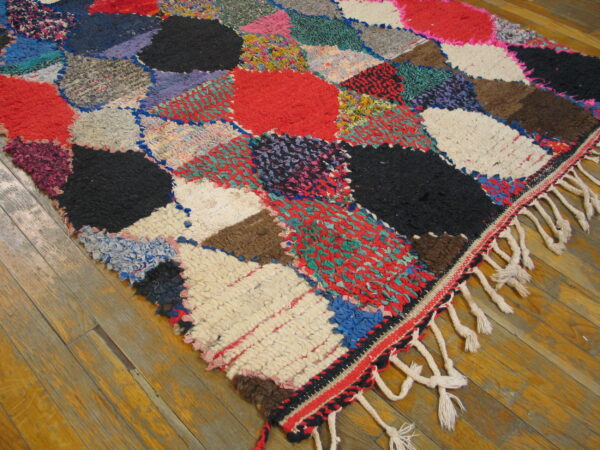 Textured multicolor patchwork rug with large shaggy shapes and knotted fringe on a wood floor.