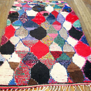 A shaggy multicolored rug with large diamond patterns in red, black, and white rests on wood plank flooring.