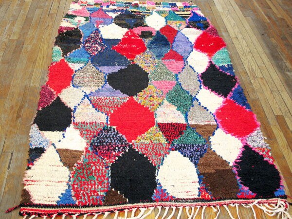 A shaggy multicolored rug with large diamond patterns in red, black, and white rests on wood plank flooring.