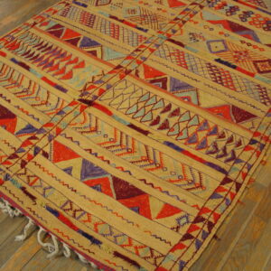 Flatwoven rug in tan, red, purple, and blue geometric patterns rests on angled wood plank flooring.