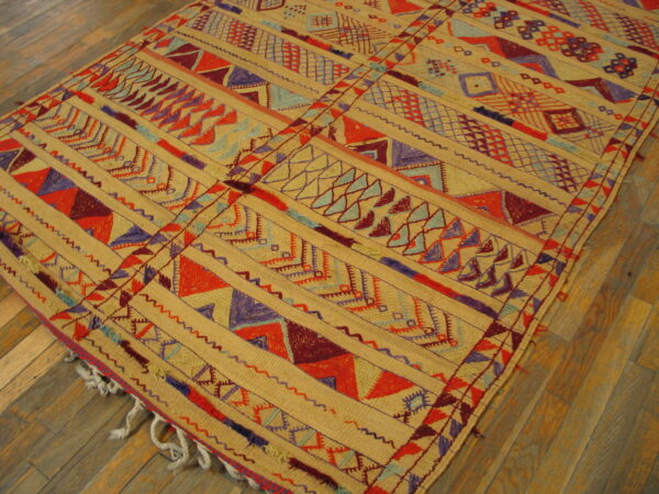 Flatwoven rug in tan, red, purple, and blue geometric patterns rests on angled wood plank flooring.