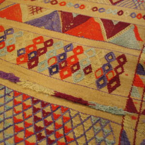 Detailed view of a tan textile with colorful geometric bands of orange, purple, red, and blue geometric patterns.