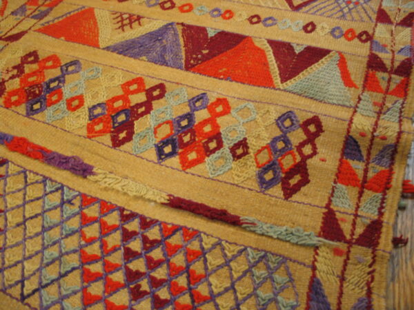 Detailed view of a tan textile with colorful geometric bands of orange, purple, red, and blue geometric patterns.