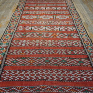 Geometric runner rug with red, white, green, and orange stripes lies on weathered wooden planks.
