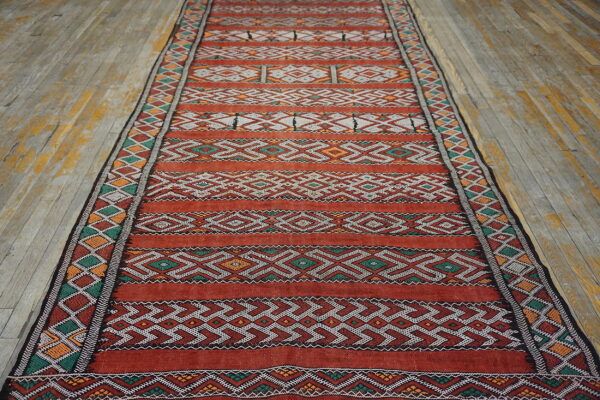 Red runner with geometric stripes in white, green, and orange lies on weathered wood floorboards.