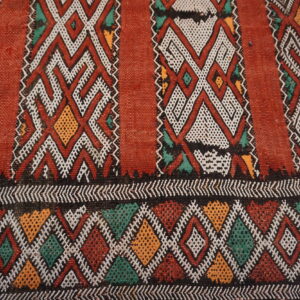 Rust and black rug detailed with white, yellow, and teal geometric diamonds and vertical zigzag stripes.