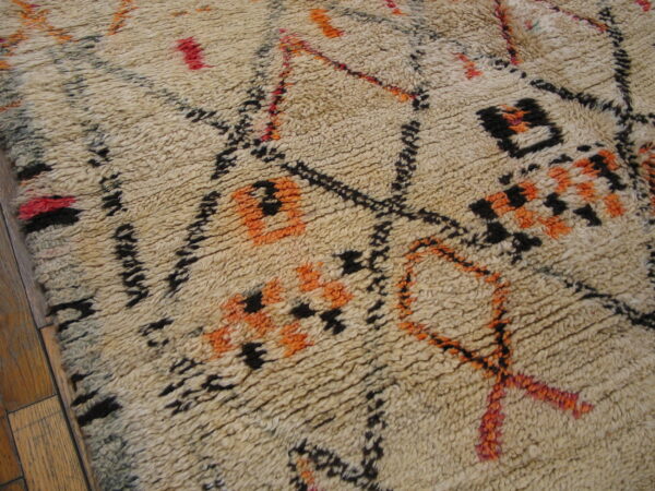 Shaggy cream rug featuring abstract motifs in black, bright orange, and red over wood flooring.