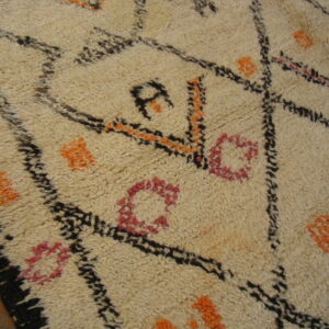 High pile cream rug with black geometric lines and orange and pink details on a dark wood floor.