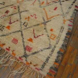 Shaggy cream rug featuring an abstract diamond pattern in black, orange, and red on dark wood planks.