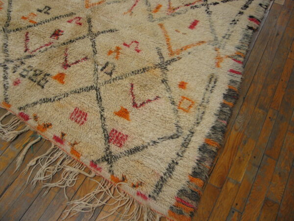 Shaggy cream rug featuring an abstract diamond pattern in black, orange, and red on dark wood planks.