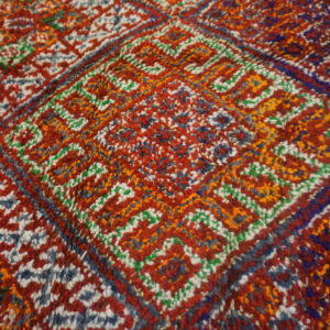 Visible thick-pile rug texture showing geometric designs colored primarily in red, orange, blue, and white.