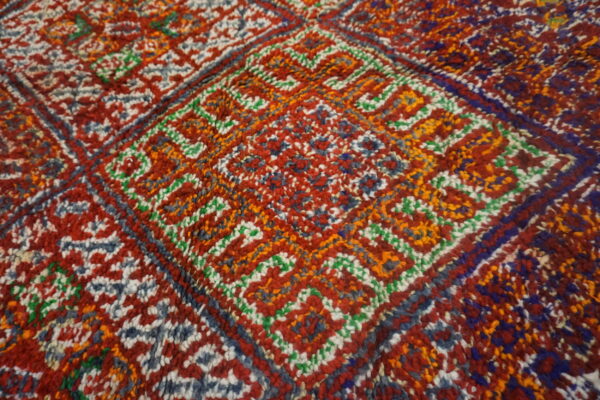 Visible thick-pile rug texture showing geometric designs colored primarily in red, orange, blue, and white.