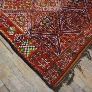 High-pile red rug featuring colorful geometric patterns and dark tassels on distressed gray wood flooring.