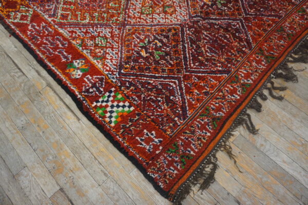 High-pile red rug featuring colorful geometric patterns and dark tassels on distressed gray wood flooring.