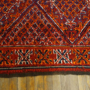 Textured red rug featuring blue, orange, and white tribal diamonds and a patterned border on wood.