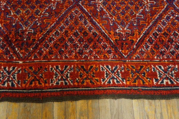 Textured red rug featuring blue, orange, and white tribal diamonds and a patterned border on wood.