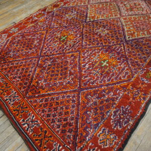 Shaggy red rug with geometric patterns in purple, orange, and white lies on distressed wood floors.