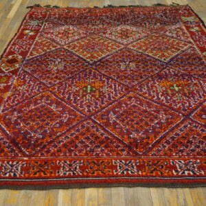 High-pile red and purple rug with a complex geometric diamond pattern resting on light brown hardwood flooring.