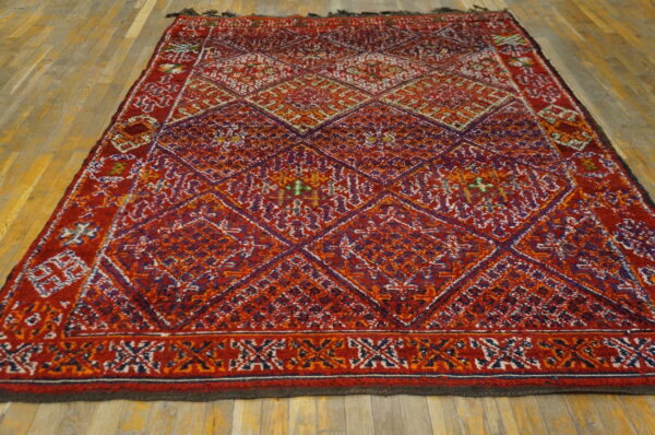 High-pile red and purple rug with a complex geometric diamond pattern resting on light brown hardwood flooring.