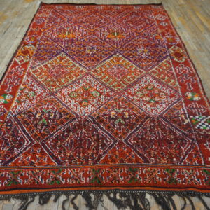 High-pile red and multi-color geometric rug featuring large diamond shapes on weathered wood flooring.