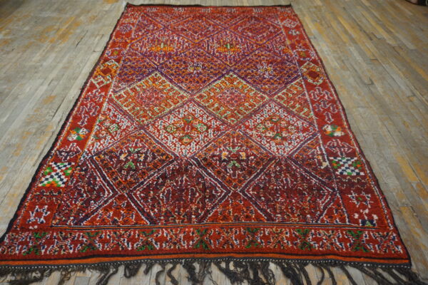 High-pile red and multi-color geometric rug featuring large diamond shapes on weathered wood flooring.