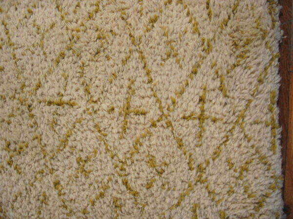 High-pile beige rug with a yellow geometric pattern, seen next to a dark wood edge.