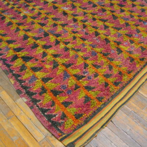 High-pile rug in pink, chartreuse, black, and orange geometric patterns on worn wooden flooring.
