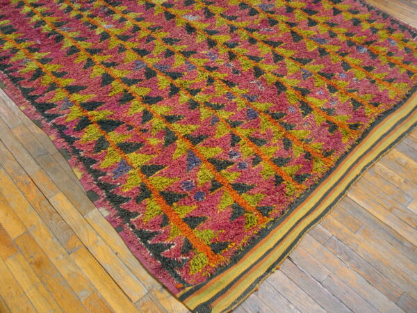 High-pile rug in pink, chartreuse, black, and orange geometric patterns on worn wooden flooring.