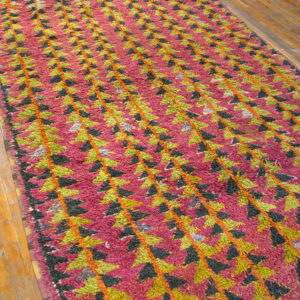 Shaggy magenta runner with repeating green, black, and orange geometric pattern on hardwood planks.