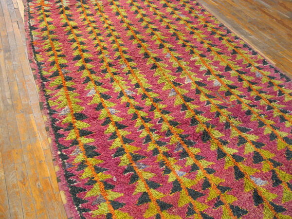 Shaggy magenta runner with repeating green, black, and orange geometric pattern on hardwood planks.