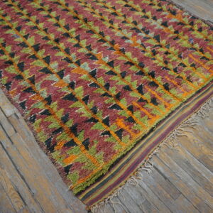 Textured rug featuring geometric triangles in maroon, lime green, black, and orange on distressed wood floors.