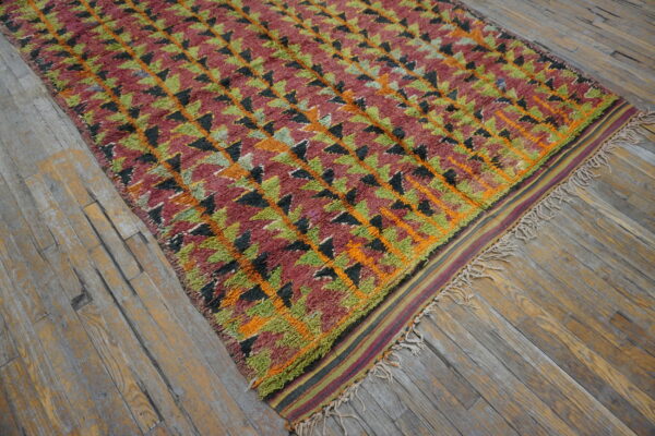 Textured rug featuring geometric triangles in maroon, lime green, black, and orange on distressed wood floors.