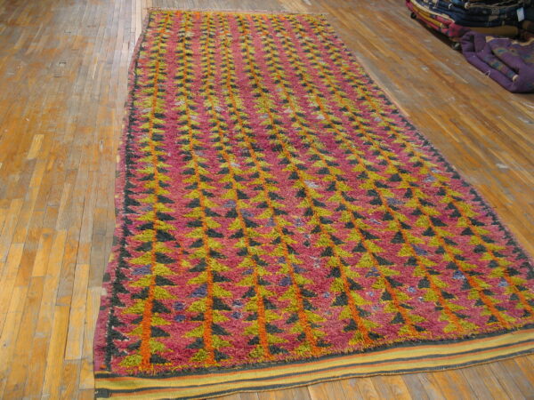 High-pile rug with pink, lime green, and black triangles arranged in vertical rows on hardwood floor.