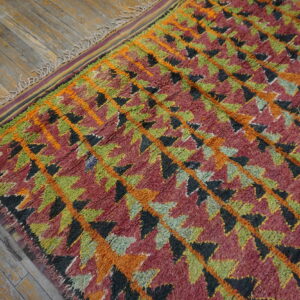 Textured high-pile rug with geometric diamonds in orange, green, red, and black on a wooden floor.