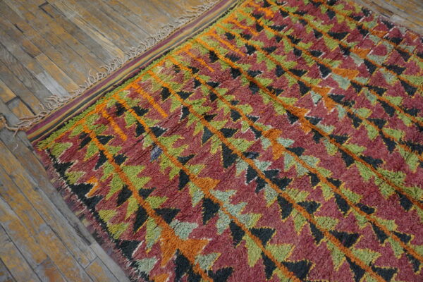 Textured high-pile rug with geometric diamonds in orange, green, red, and black on a wooden floor.
