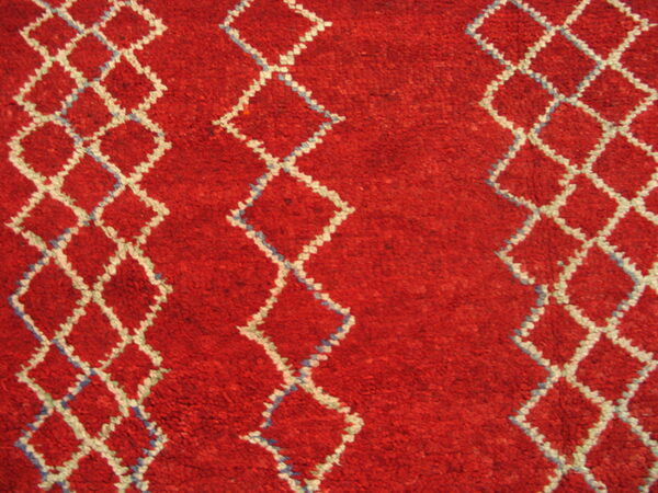 A textured red rug has white diamond patterns accented with light blue stitches.