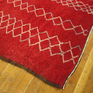 Thick, red, high-pile rug featuring white diamond patterns rests on honey-toned wood planks.