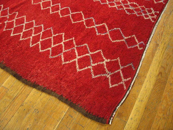 Thick, red, high-pile rug featuring white diamond patterns rests on honey-toned wood planks.