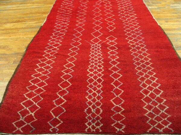 High-pile red rug featuring vertical columns of white diamond patterns on a light wood plank floor.