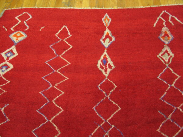 Textured red rug with white and blue geometric diamonds displayed on wood flooring.