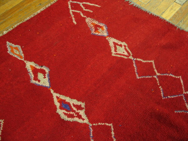 High-pile red rug featuring geometric diamond patterns in white, blue, and orange on wood flooring.