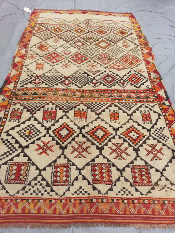 High-pile rug with an off-white field and complex geometric designs in black, red, and orange.