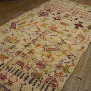 Long-pile off-white rug with scattered pink, green, and purple geometric designs on rustic wood planks.