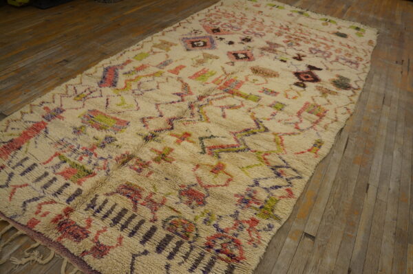 Long-pile off-white rug with scattered pink, green, and purple geometric designs on rustic wood planks.