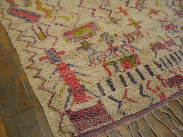 Shaggy off-white rug displaying abstract geometric patterns in pink, purple, and olive green on wood floor.