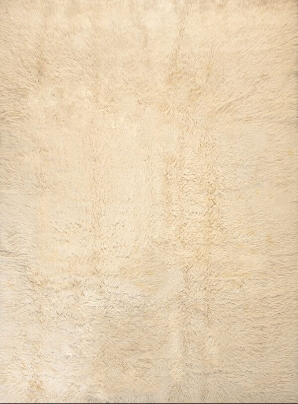Close-up texture of a solid cream-colored rug featuring a deep, plush, shaggy pile.