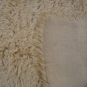 The rug's long, creamy white shag pile contrasts sharply with its smooth, light beige backing.
