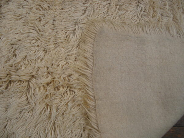 The rug's long, creamy white shag pile contrasts sharply with its smooth, light beige backing.