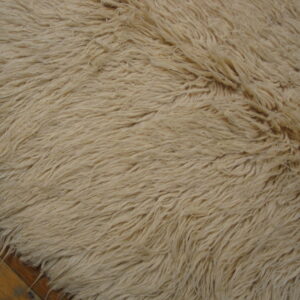 Close-up of a high-pile cream shag rug detail lying over visible brown plank hardwood flooring.