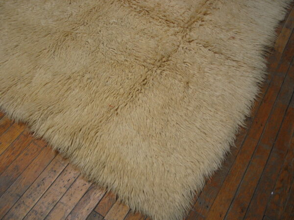 High-pile beige shaggy rug placed corner-down on dark, rustic wood planks.